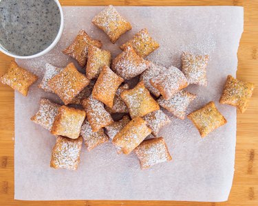 Dozens of mini Black Sesame Mochi Beignets on a piece of parchment paper, dusted with black sesame powder