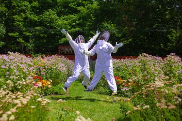 Two people in white beekeeping suits jumping for joy in a garden