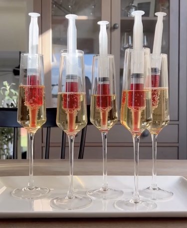 Glasses of champagne containing red juice-filled syringes