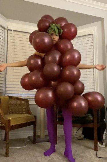 Woman wearing purple tights and a costume made from purple balloons to resemble grapes