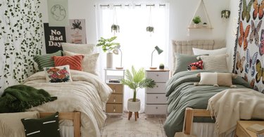 A college dorm room with two twin beds, one has a cream-colored tufted headboard and there is lots of wall decor and faux plants.