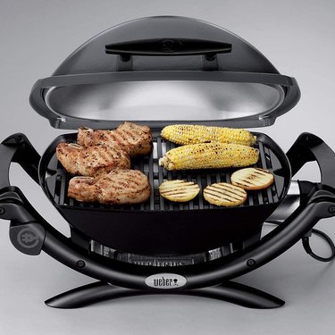 Compact Weber electric grill, shown in use grilling three steaks, two ears of corn and three chicken patties