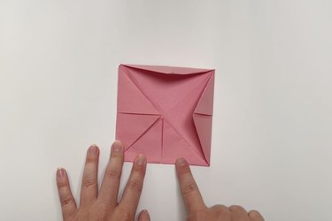 A smaller square piece of pink paper with four corners folding in to the center