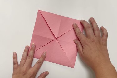 A square piece of pink paper with four corners folding in to the center