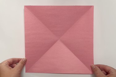 A square piece of pink paper with two diagonal creases creating an X
