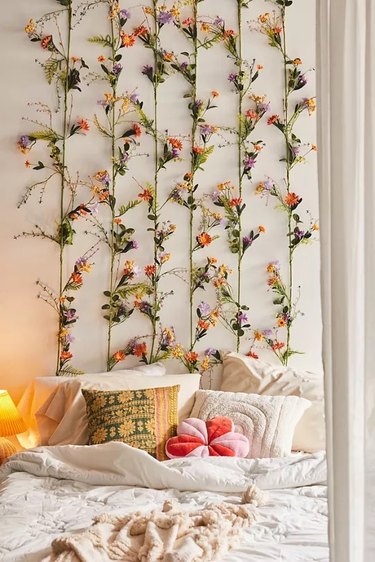 Six faux floral garlands from Urban Outfitters strung vertically behind a bed with lots of throw pillows.