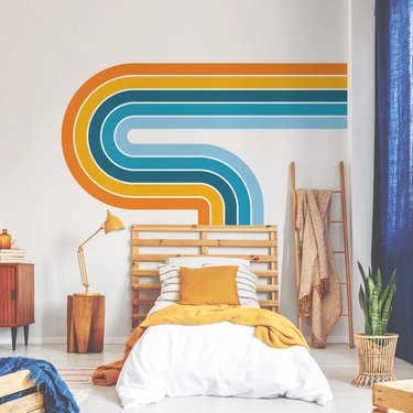 Curvy, retro wall decal on a wall behind a bed in shades of blue, yellow, and orange.