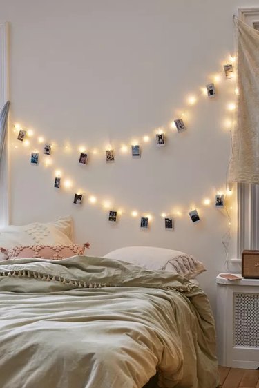Two sets of string lights with clips for attaching small photos on a wall behind a bed.
