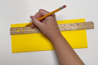A hand making a pencil mark where a ruler indicates 2 1/8 inches