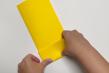 Two hands folding a piece of yellow paper into small rectangles