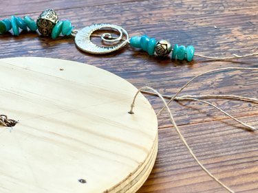 thread strings of wooden beads through the outer holes in the wooden disc