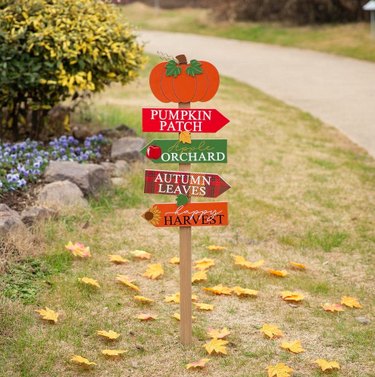 Fall Wooden Pumpkin Patch Yard Stake from Home Depot in the grass. There are directional pointers to the pumpkin patch, orchard, autumn leaves, and happy harvest.