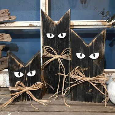 Three handmade wooden black cats from Etsy with pointy ears and jute ribbon bows around their necks.