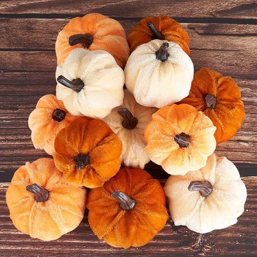 A dozen or so Velvet Foam Pumpkins from Amazon in colors white, light orange, and dark orange on a wooden table pictured from above.