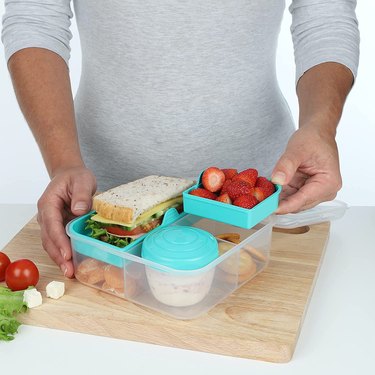 Anonymous person showing off the different compartments in the Sistema To Go Bento Lunch Box. There's a cup-shaped container with a lid for holding salad dressing.
