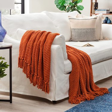 Textured Knitted Super Soft Throw Blanket with Tassels from Amazon pictured in orange draped over the arm of a white sofa.