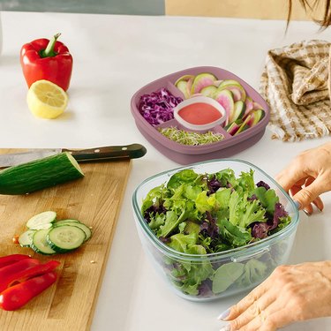 Anonymous person using the Bentgo Glass And Silicone Salad Container with greens on the bottom and salad toppings and dressing in the top compartment, all separated to ensure freshness.