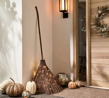 Witch's broom with wood handle and LED lights in the 'straw' end, leaning against a wall near a front door.