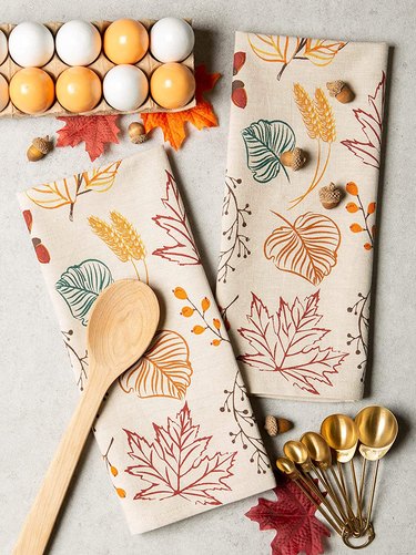 Autumn Leaves Printed Dish Towel Set from Amazon. The fabric is off-white and it's printed with autumn leaves in orange, green, yellow, and red.