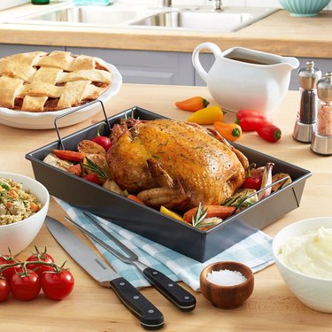 Chicago Metallic 9X13 rectangular roaster, pictured on a butcher block countertop with a roasted turkey surrounded by roasted veg, and a pie, gravy boat and carving utensils in the foreground