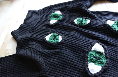 Black knit sweater with green eyes laid out on a flat surface