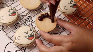 Piping ring of chocolate ganache on macaron shell.