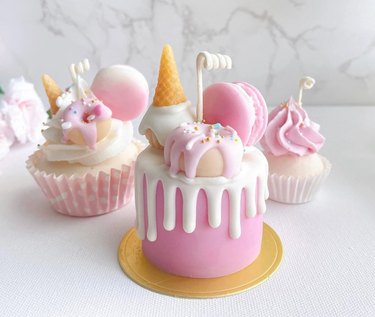 Three candles shaped like light pink and white cupcakes, cake, macarons and ice cream cones