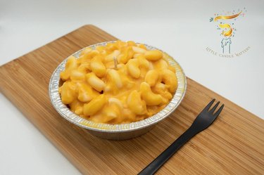 Candle shaped like orange mac and cheese in a silver container