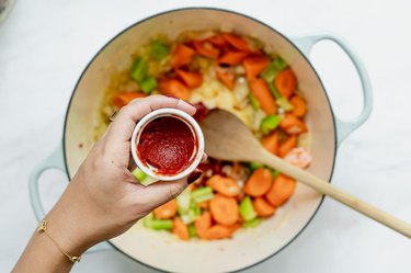 adding tomato paste to vegetables.