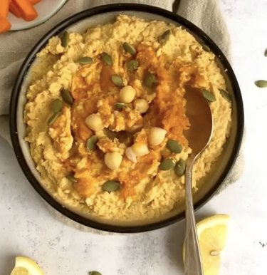 Bowl of pumpkin hummus topped with seeds and chickpeas