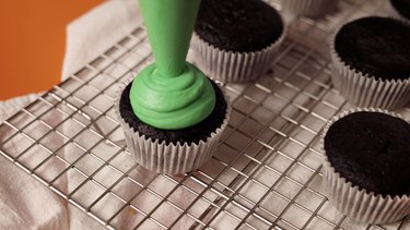 Piping green frosting on top of cupcake