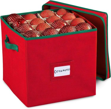 Red ornament storage box made of fabric with a matching lid, green handles, and a spot to put a label.