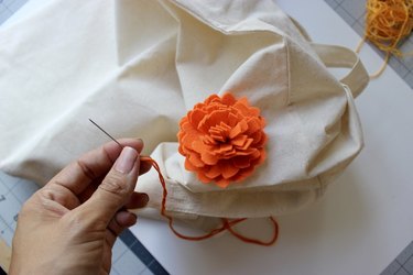 Orange felt marigold being sewn onto tote bag