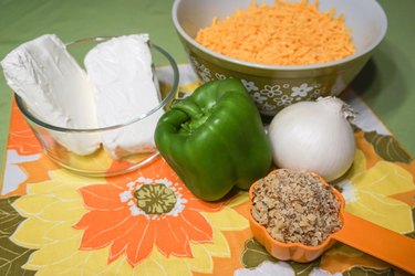 Shredded cheddar cheese, cream cheese, a yellow onion, a green bell pepper, and chopped walnuts paired with an orange and gold floral napkin