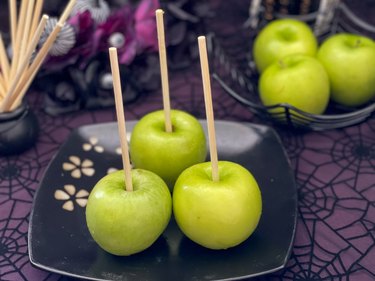 3 green Granny Smith apples on a black plate with wooden sticks