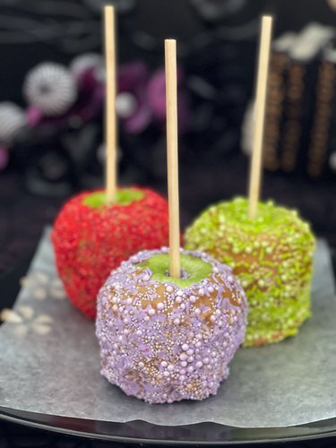 3 caramel apples rolled in purple, red, and green candy sprinkles
