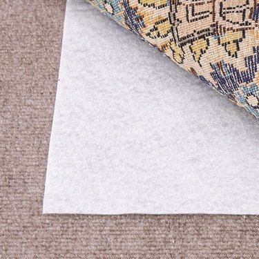 White rug pad between tan carpet and a multicolored area rug.