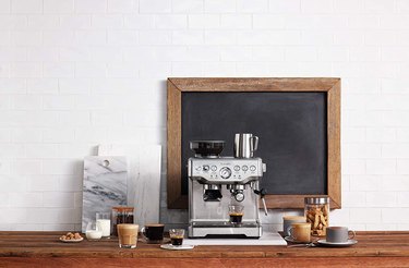 Breville espresso machine on a wood countertop against a white brick wall.