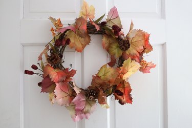 Fall wreath with autumnal leaves hanging on white door