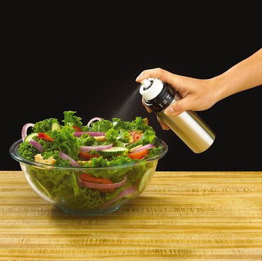 Person using Misto bottle to spray olive oil on a salad.