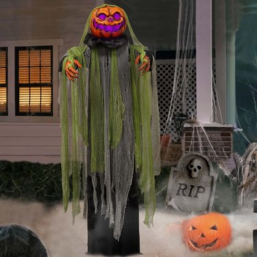 Pumpkin head root of evil in fog machine. It has outstretched arms and green and gray gauzy material that hangs down like a cloak.