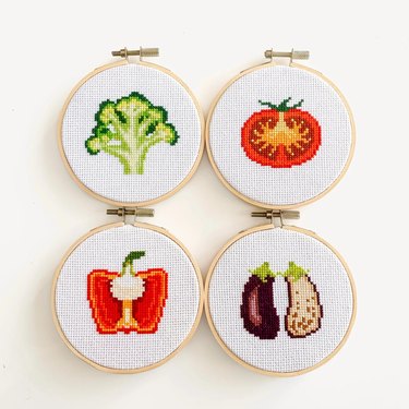 White circular cross-stitch patterns featuring broccoli, a tomato, a red pepper and an eggplant cut in half