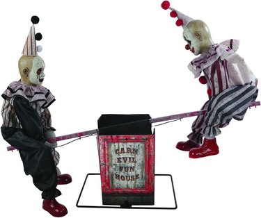 Two child-sized clowns on a see-saw that reads "Cars Evil Fun House."
