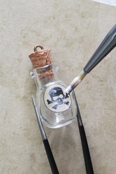 Applying skull and crossbones label on a glass bottle pendant