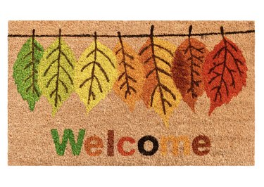 Coir doormat with colorful fall leaves hanging from a line and the phrase "Welcome" in matching colors.