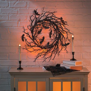 Twig wreath with LED lights and decorative, glittery bats above a media console.