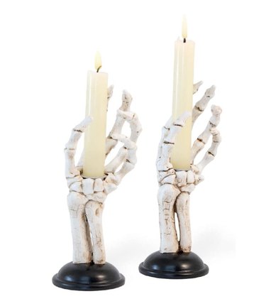 Skeleton hand taper candle holders mounted to black stands.