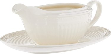 A white stoneware gravy boat on a saucer, both with an elegant fluted design