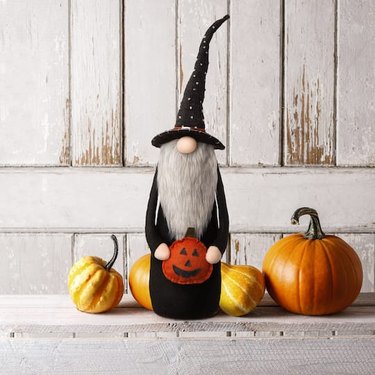 Stuffed Halloween gnome wearing a wizard hat and holding a felt jack-o'-lantern.