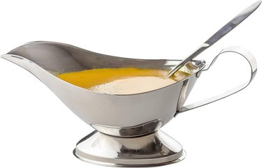 A stainless steel gravy boat with a broad pour spout and a stainless steel ladle